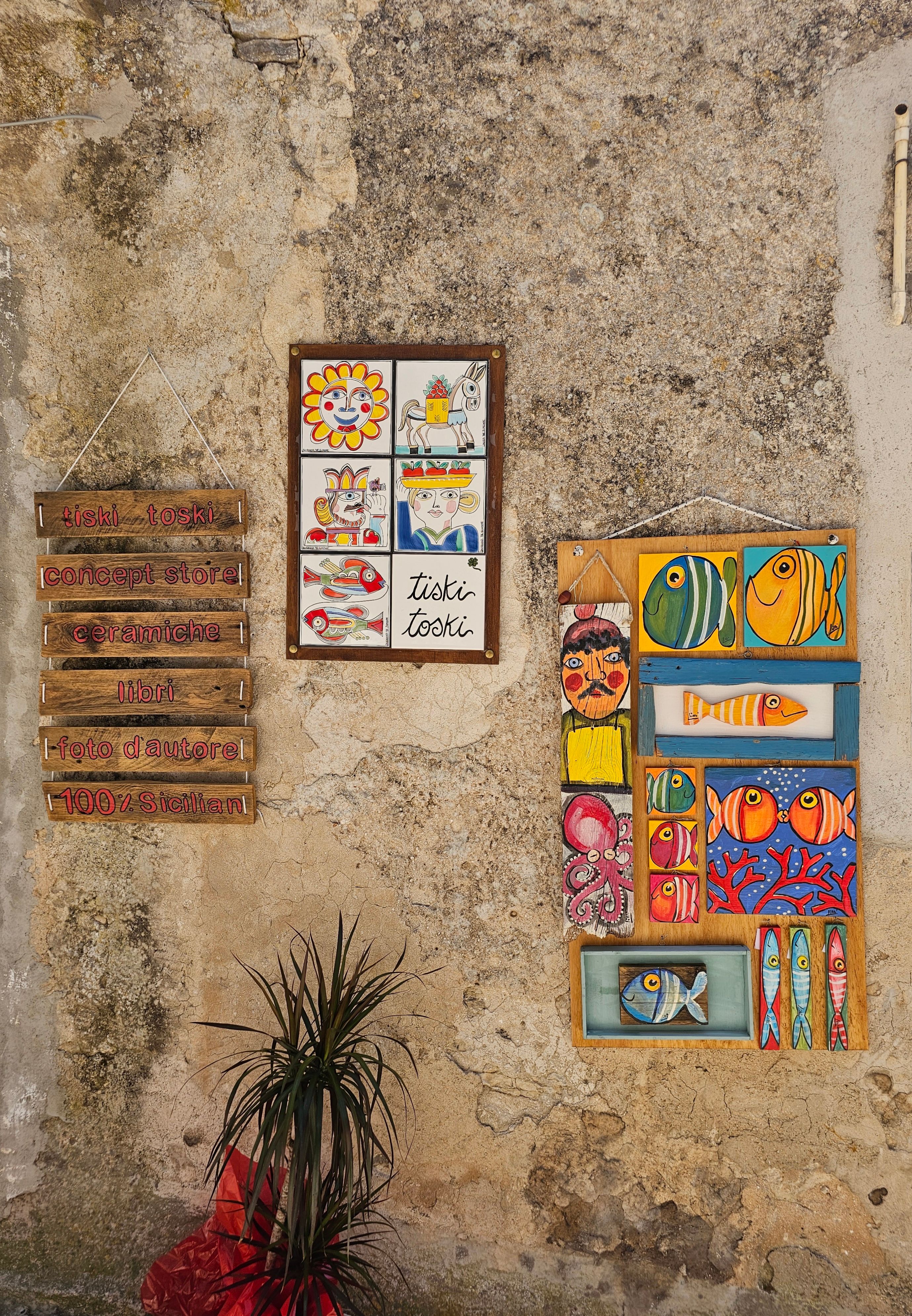 Vibrant ceramic artwork on rustic wall in Erice, Sicily, featuring colorful fish and plaques.
