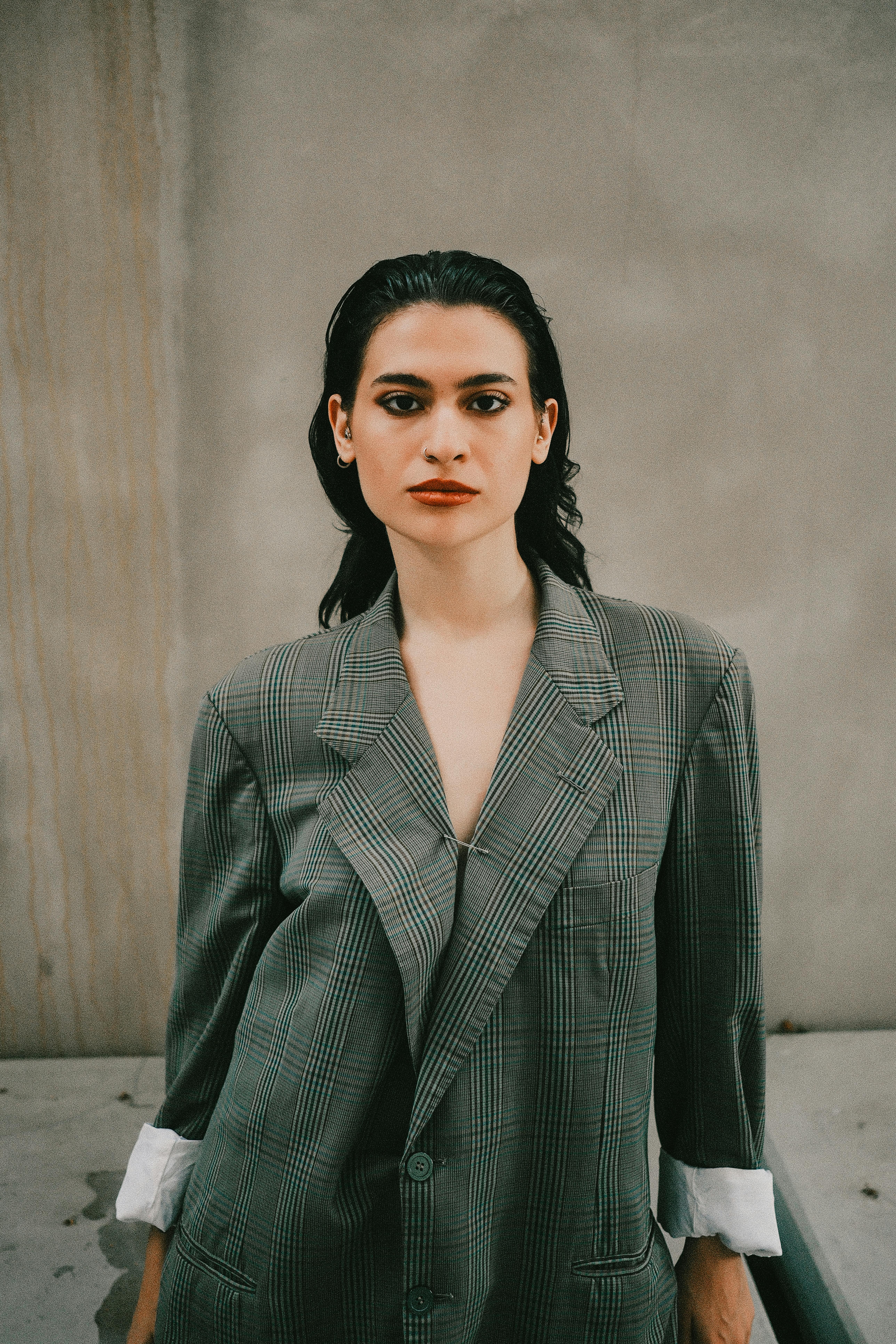 Confident woman wearing oversized plaid coat posing against neutral wall.