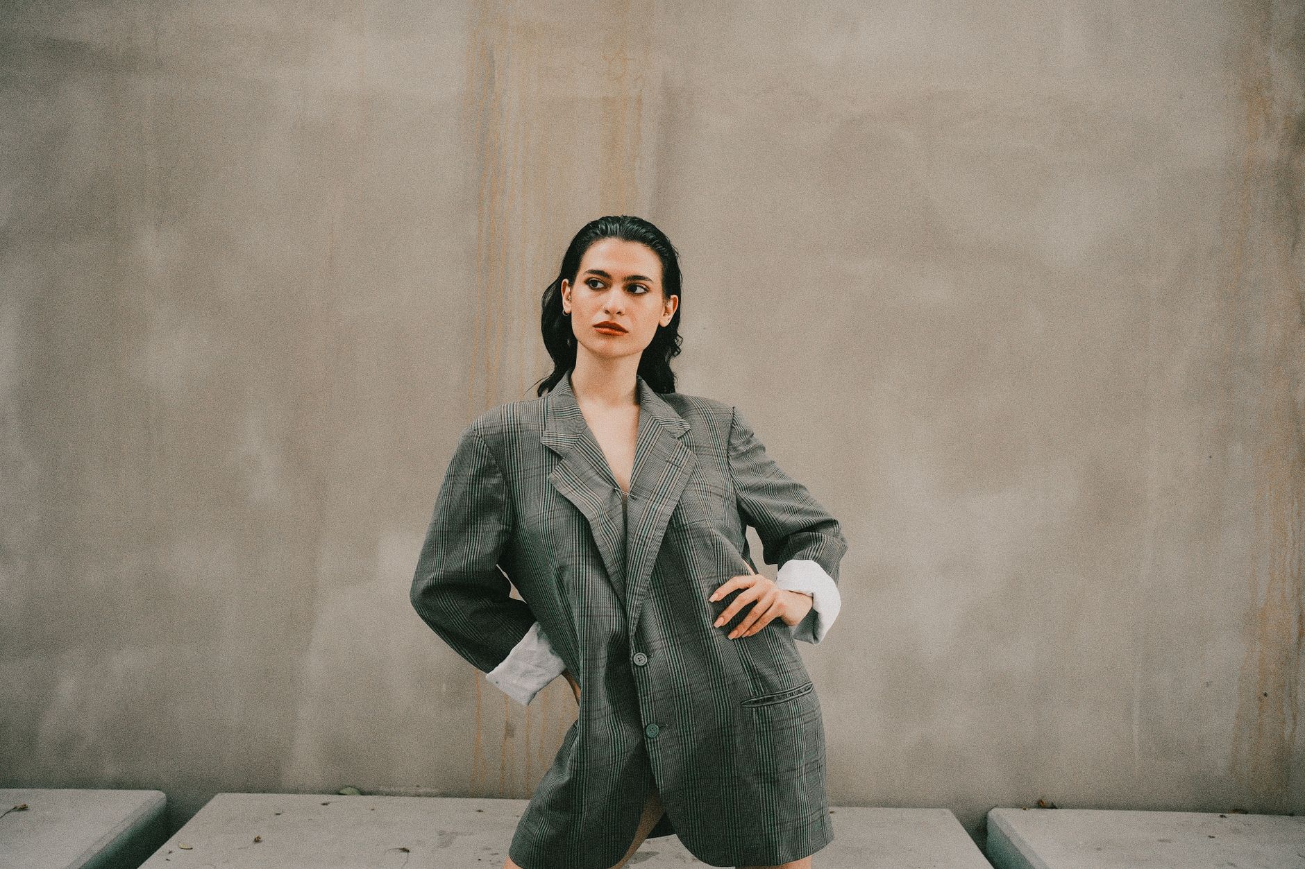Femme en blazer oversize à carreaux posant devant un mur béton, style veste grande taille urbain
