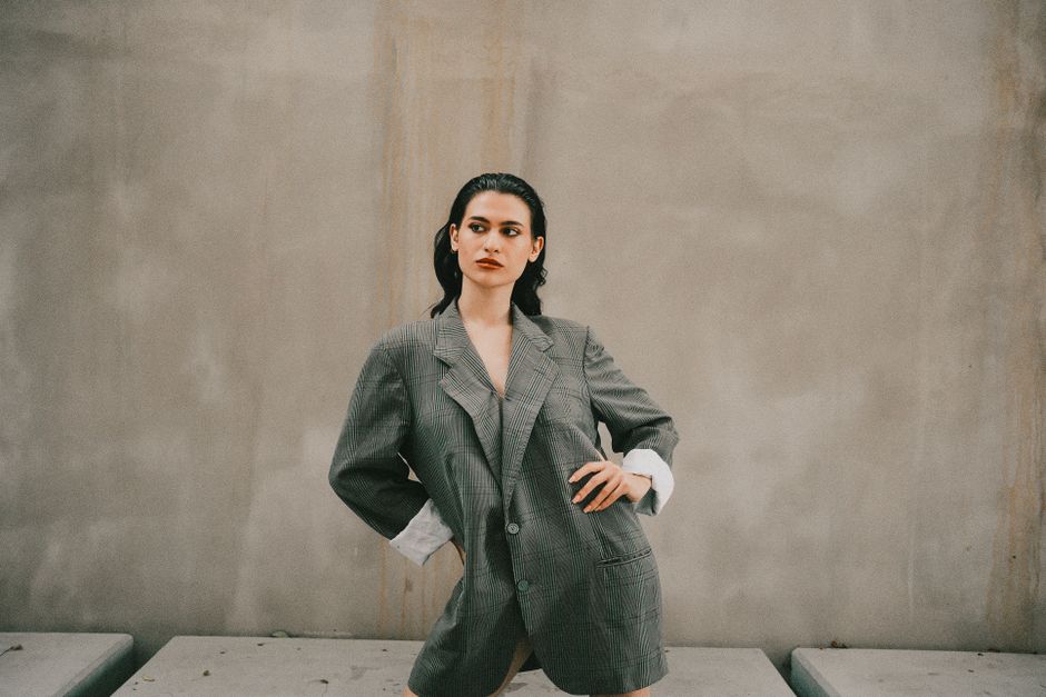 Stylish woman posing in oversized suit against minimalist backdrop.