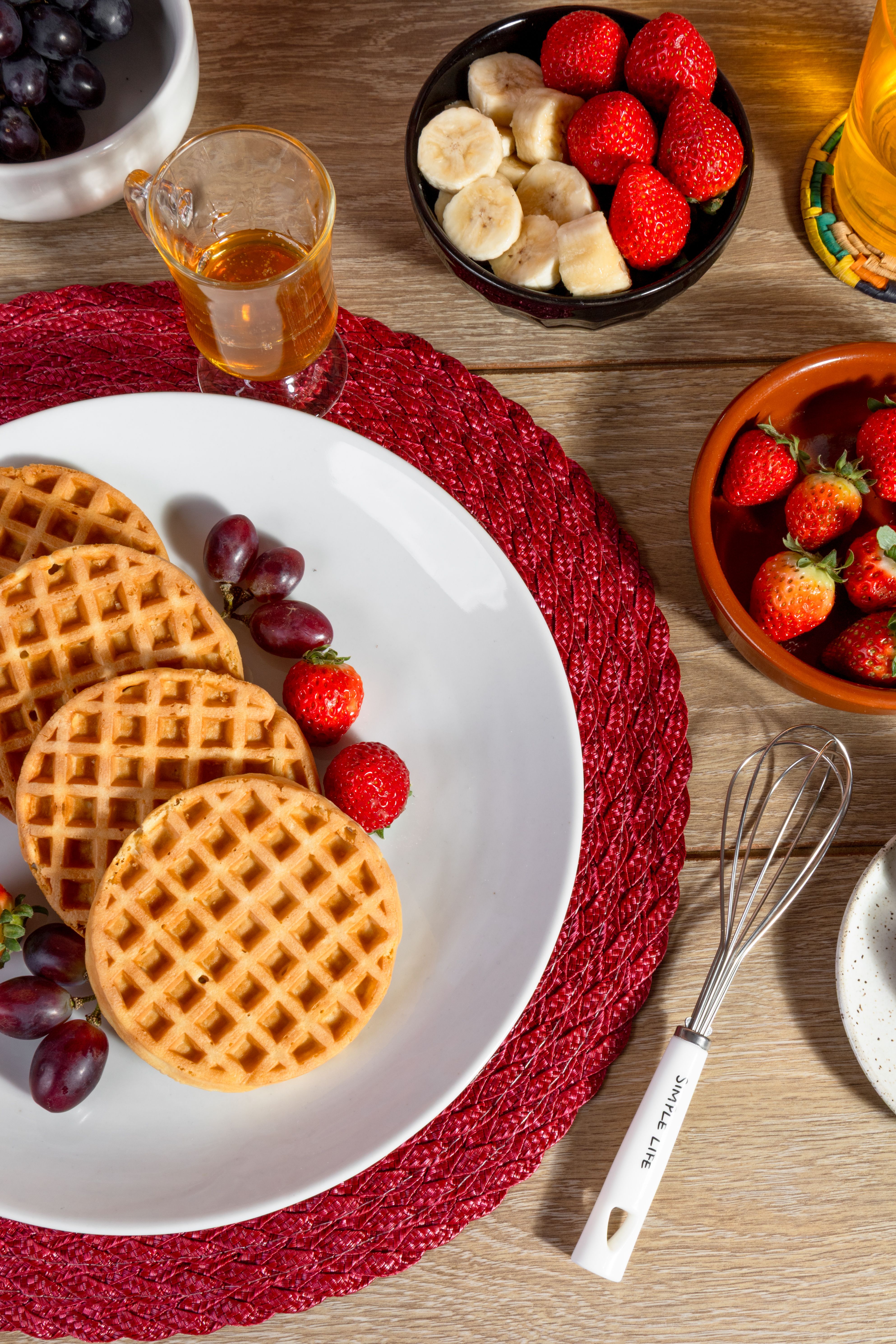 Top view of waffles with fresh strawberries, bananas, grapes, and maple syrup on a breakfast table.