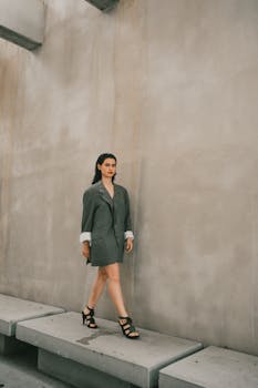 Stylish woman in blazer and heels walking against a modern concrete wall.