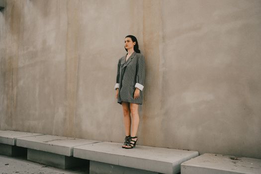 Stylish woman standing against a concrete wall, wearing an oversized blazer.