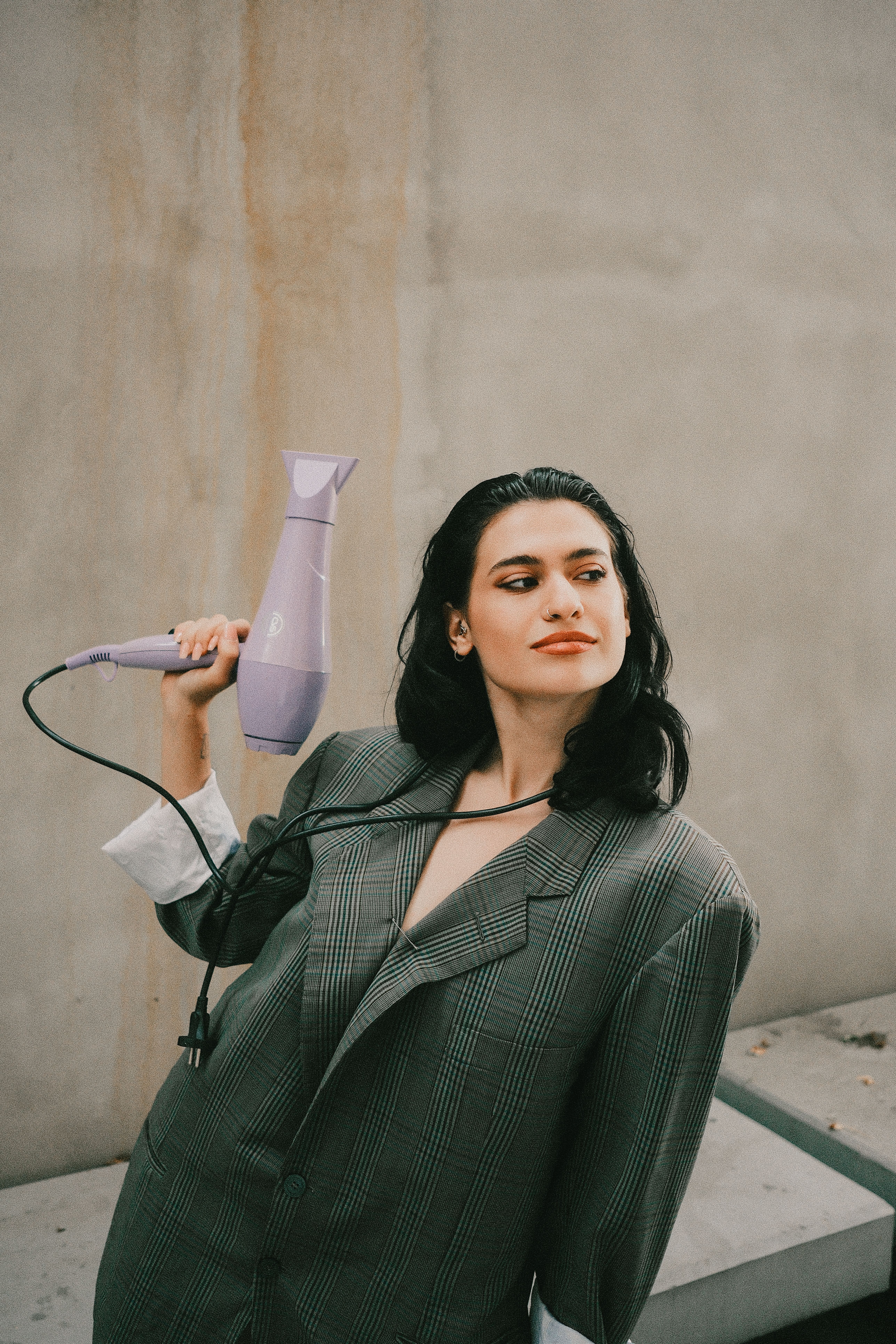 Confident woman posing with hairdryer in a fashionable oversized blazer outdoors.