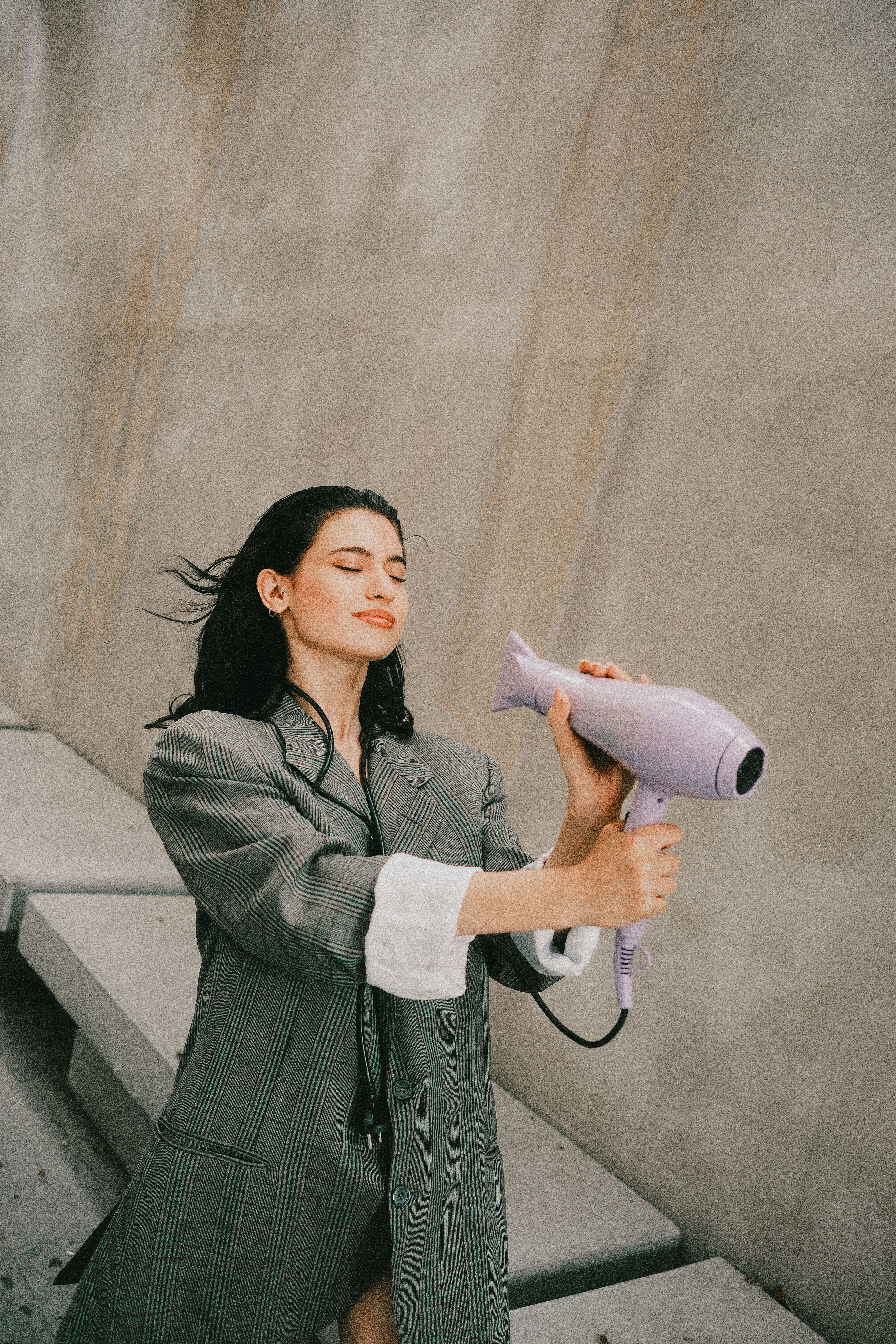 Fashionable woman using hair dryer outdoors, enjoying fresh air in style.