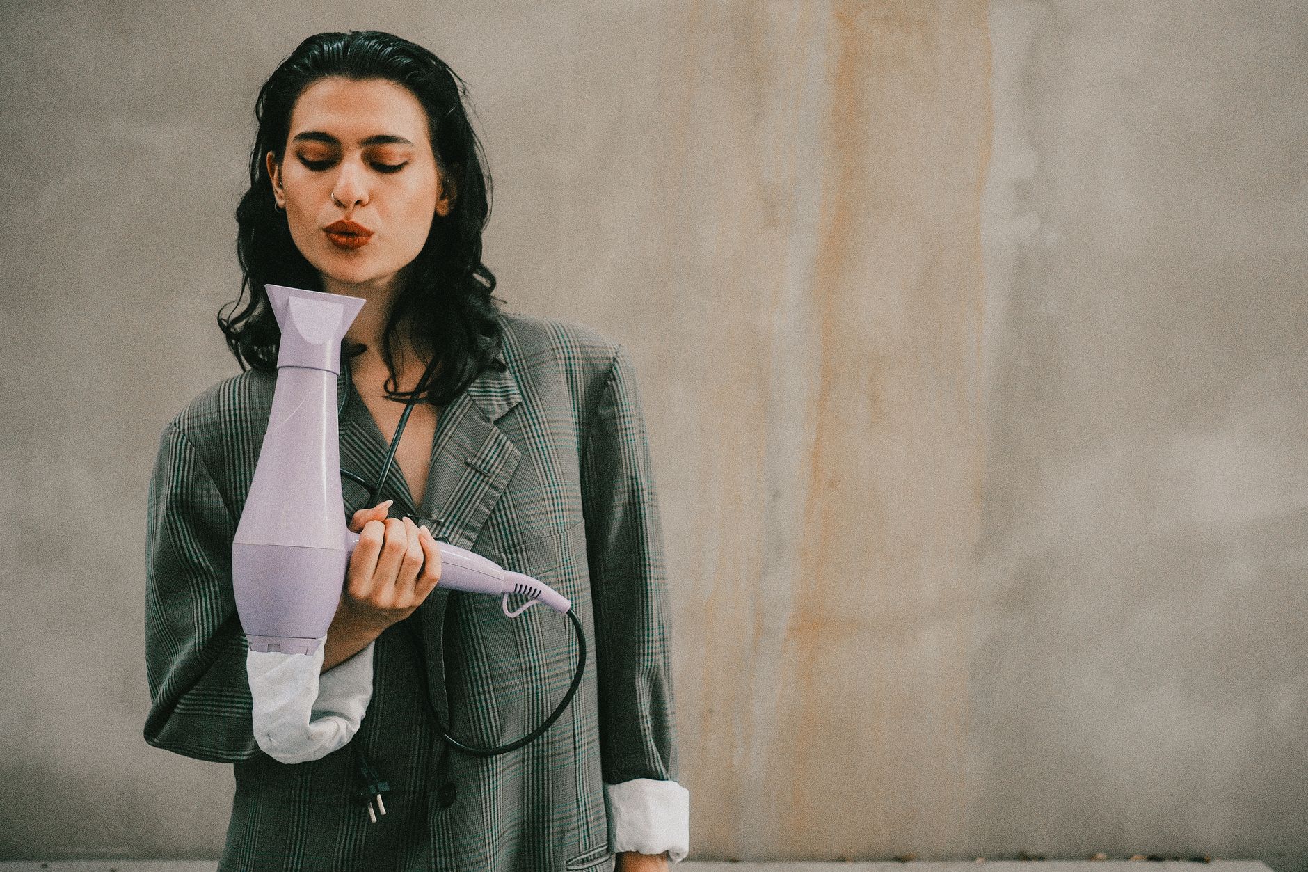 Fashionable woman posing with a lavender hairdryer in trendy blazer for an artistic portrait.