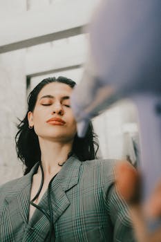 Close-up of a woman using a hair dryer in a modern bathroom setting.