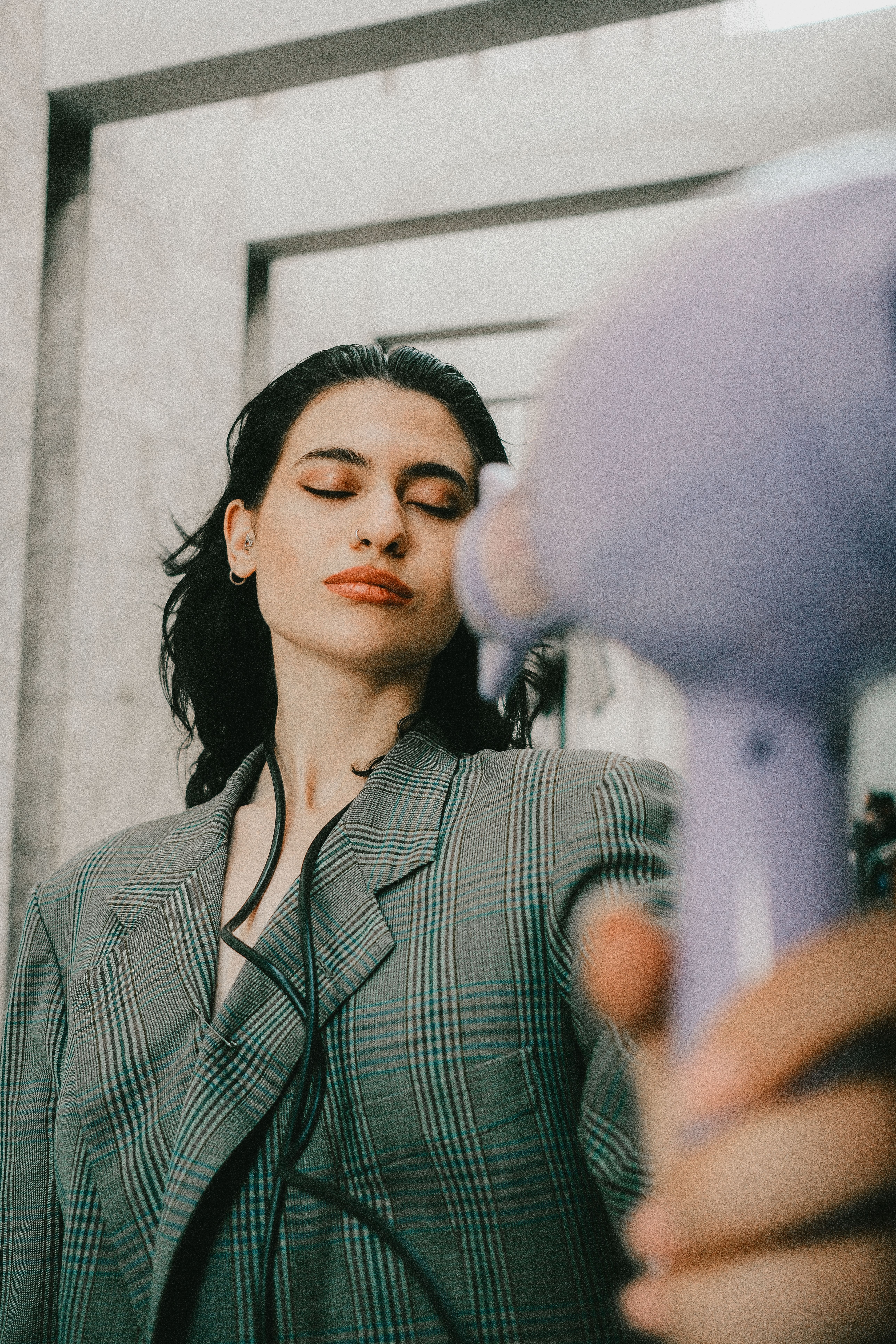 Stylish woman in blazer drying her hair with a vivid purple hair dryer.
