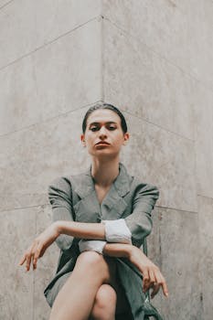 Modern portrait of a confident woman in a stylish suit seated against a stone wall.