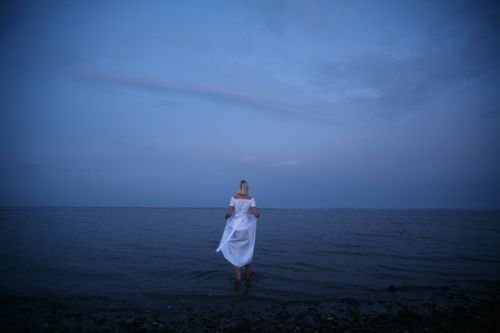 Free A woman in a white dress stands by the tranquil sea at twilight. Stock Photo