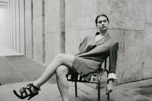 A woman in a stylish outfit sits comfortably in a minimalist urban environment.