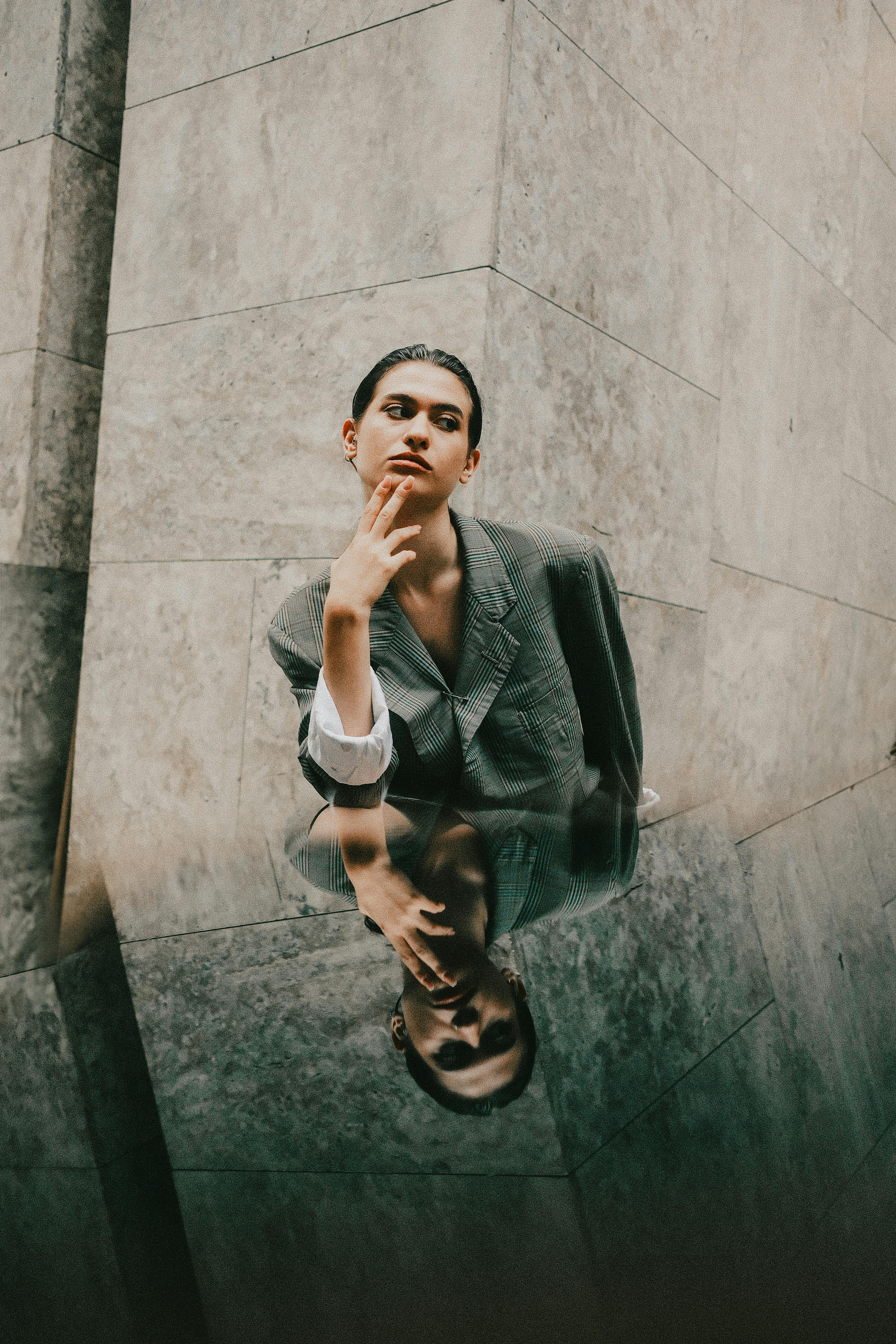 Artistic portrait of an adult in a blazer reflected on a marble surface.