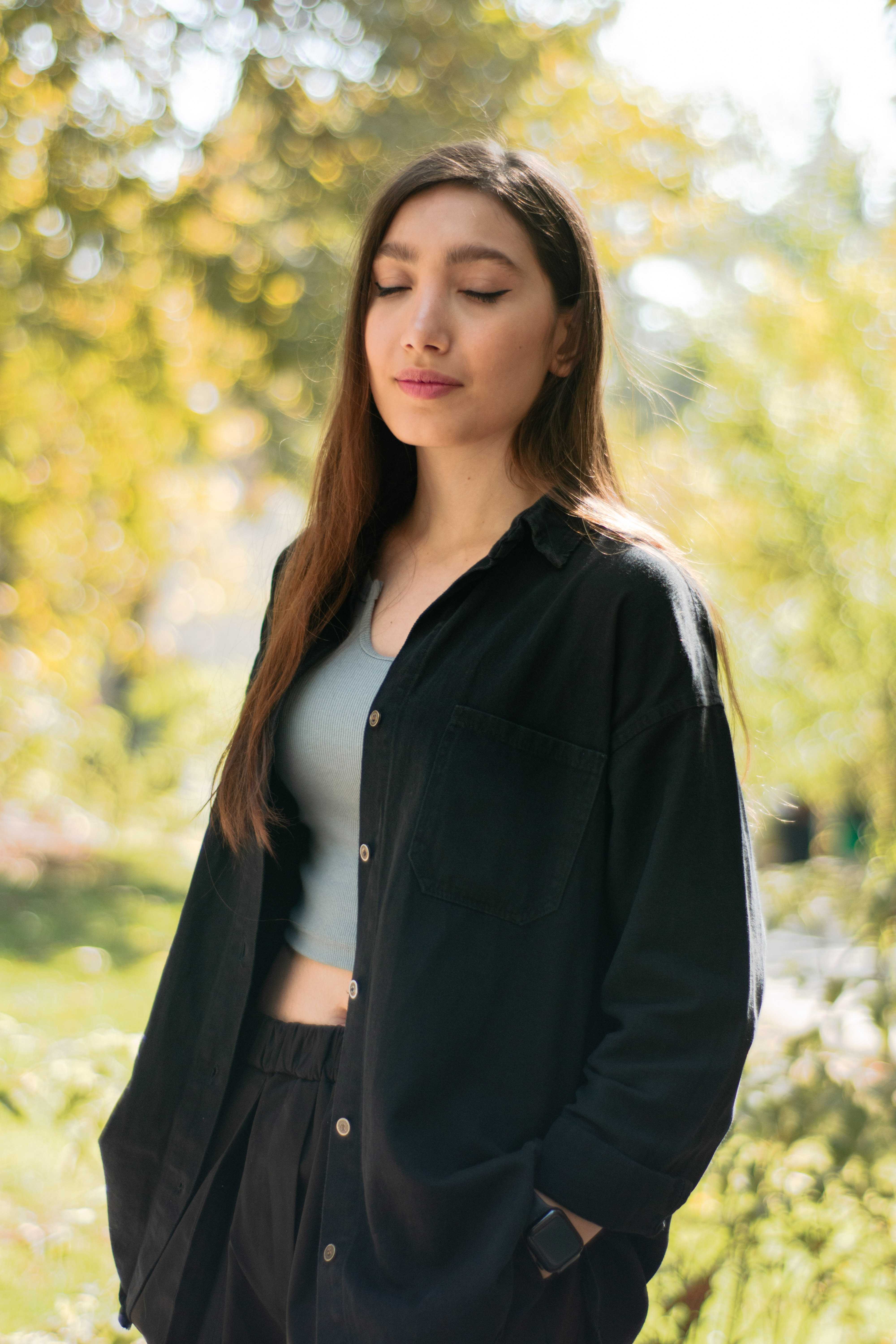 Portrait of a serene woman with closed eyes, standing outdoors in a sunlit garden.