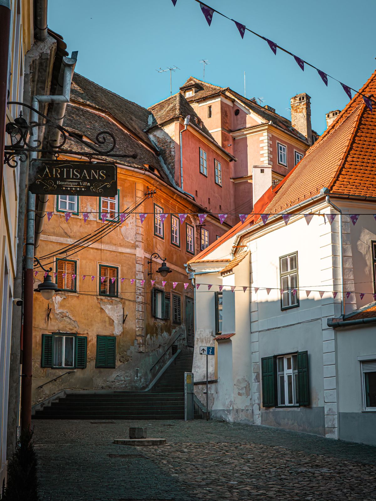 Stradă din Sibiu cu clădiri istorice colorate și o firmă de meșteșugar