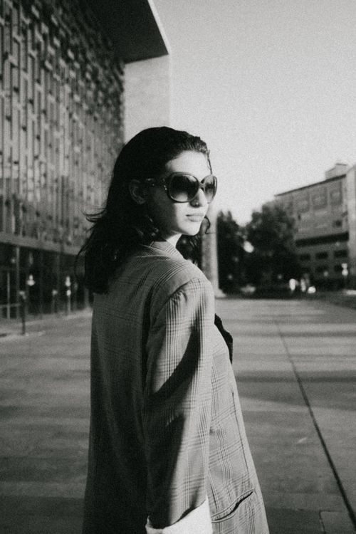 Free Monochrome image of a fashionable woman in sunglasses walking an urban street, exuding elegance. Stock Photo