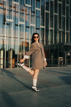 Fashionable woman posing in urban setting with glass facade.