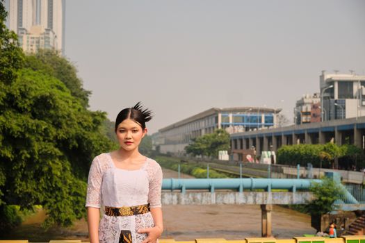 A woman in traditional attire with Jakarta's urban landscape in the background.