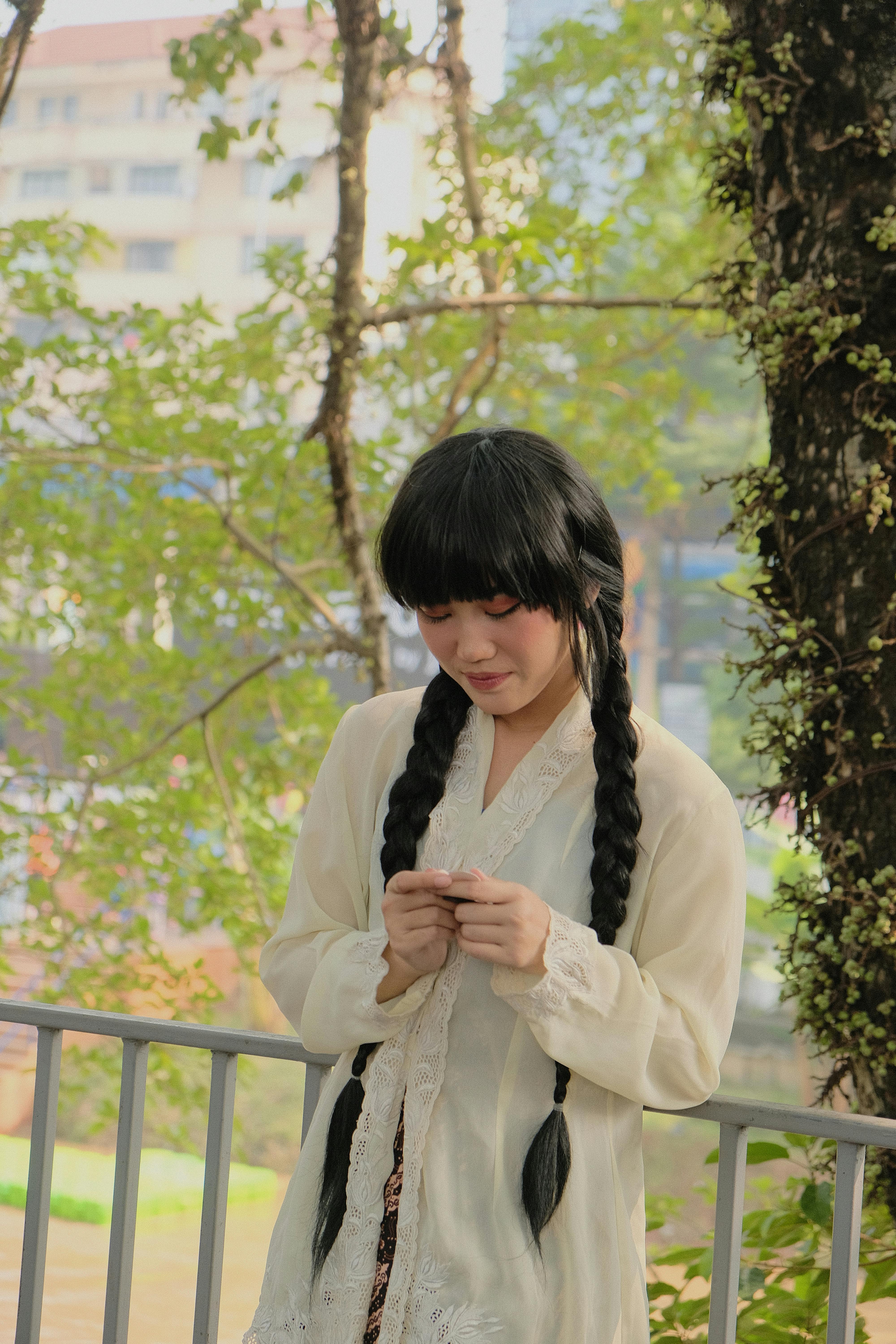 Gratuit Une jeune femme aux cheveux tressés, vêtue d'une robe traditionnelle, se tient à l'extérieur à Jakarta. Photos