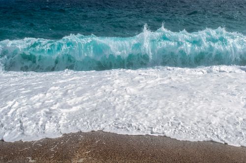 Free A powerful ocean wave crashes onto a sandy beach, capturing nature's raw beauty and energy. Stock Photo