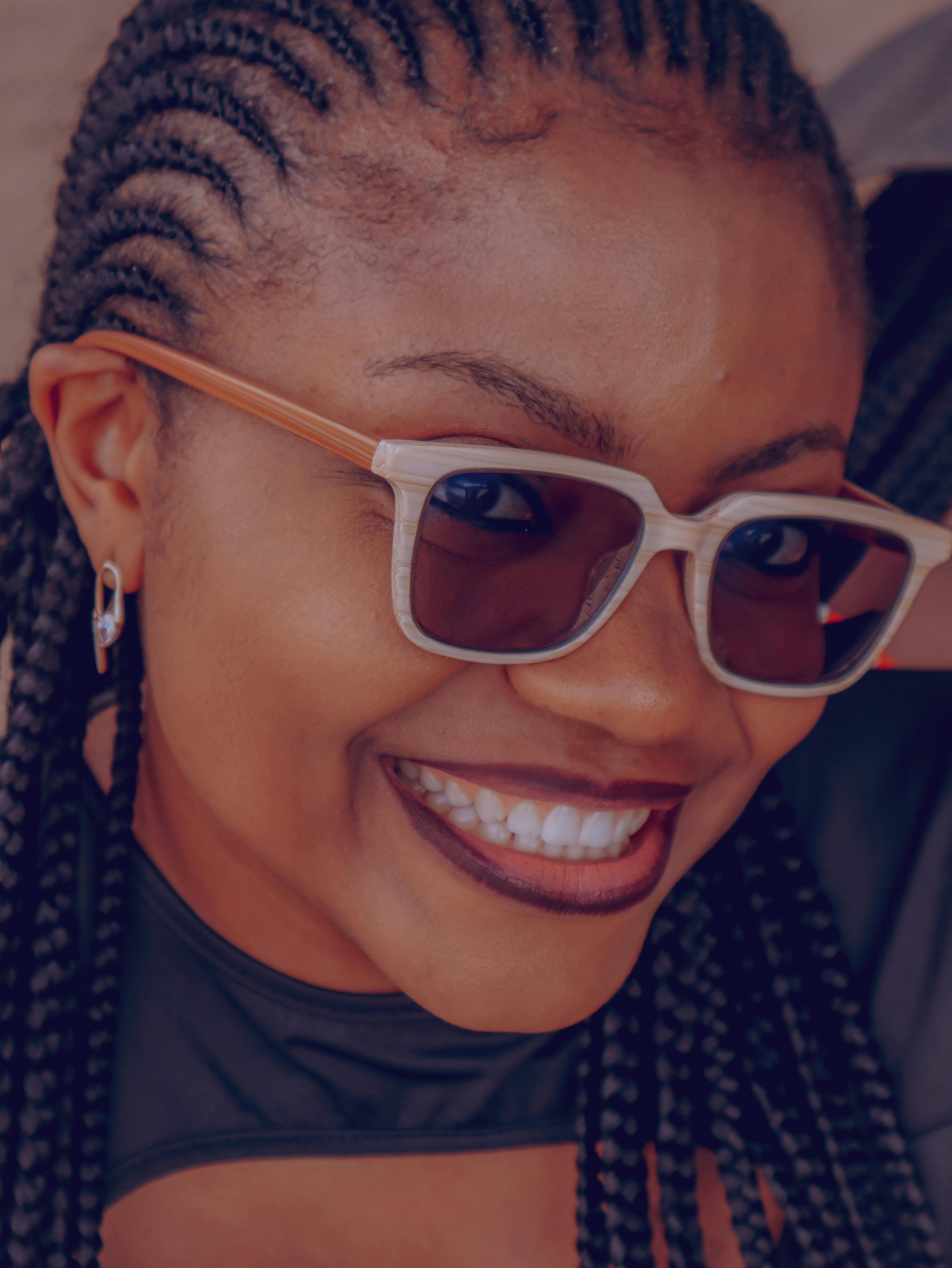 Gratuit Gros plan d'une femme souriante avec des lunettes de soleil et des cheveux tressés, capturant une ambiance vibrante à Abuja, au Nigéria. Photos