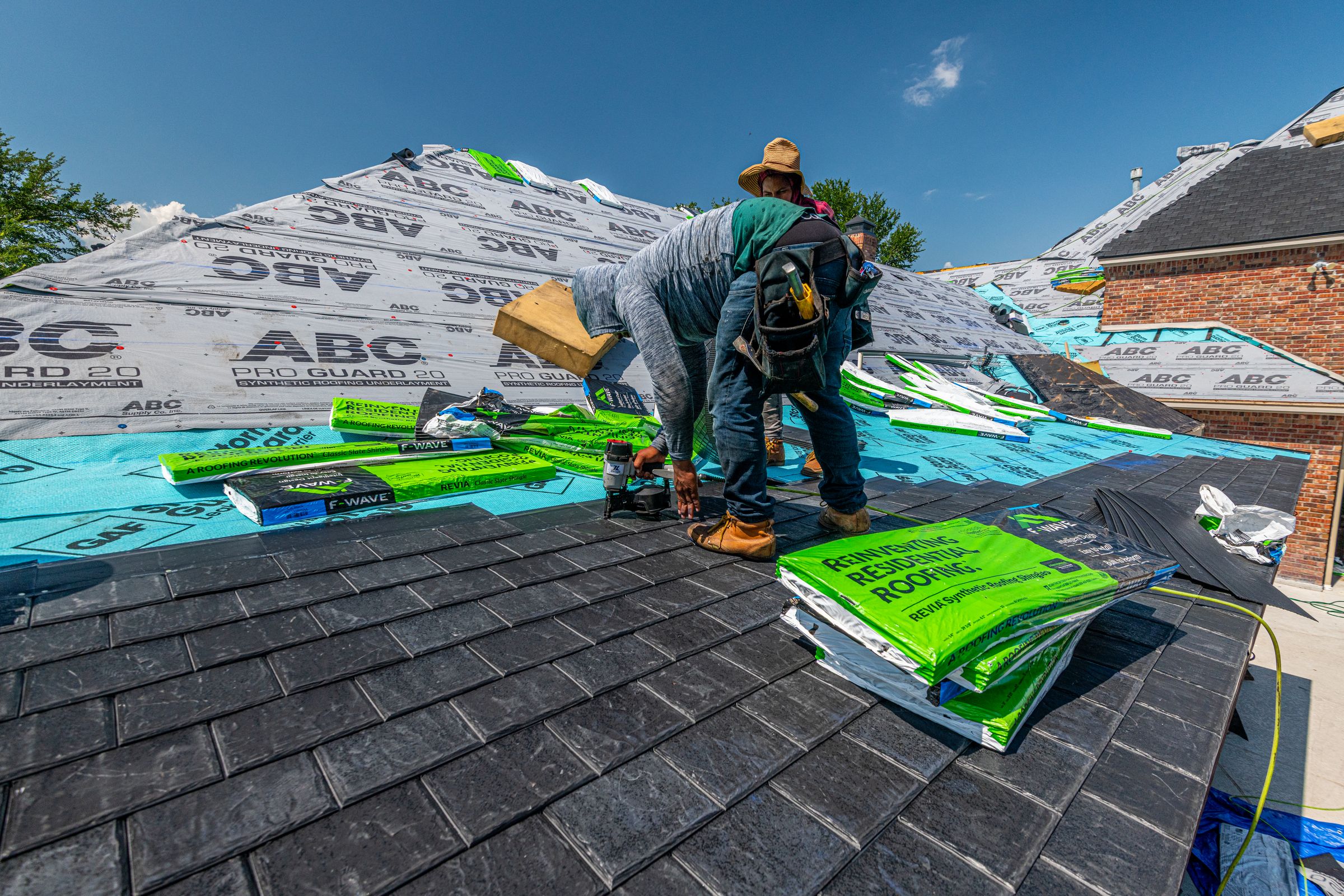 Workers installing a synthetic slate roof on a brick house