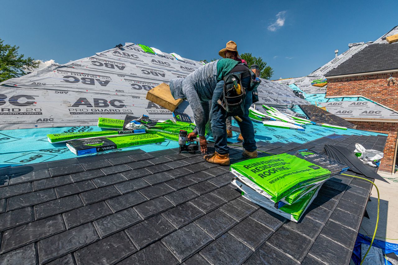 Two roofers in safety helmets repairing a roof together