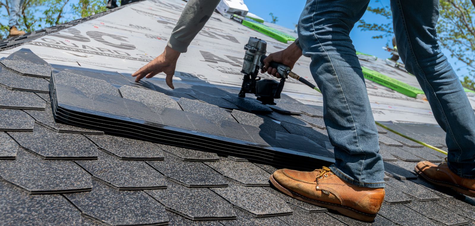Roofer using a nail gun to install shingles on a home