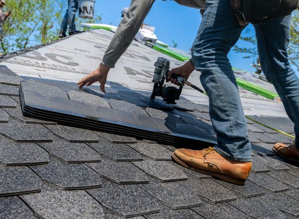 Roofer using a nail gun to install shingles on a home