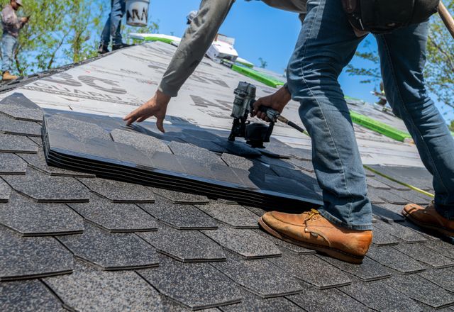 Roofer using a nail gun to install shingles on a home