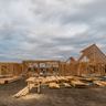The wooden frame of a large new house under construction stands beneath a heavy, overcast sky.
