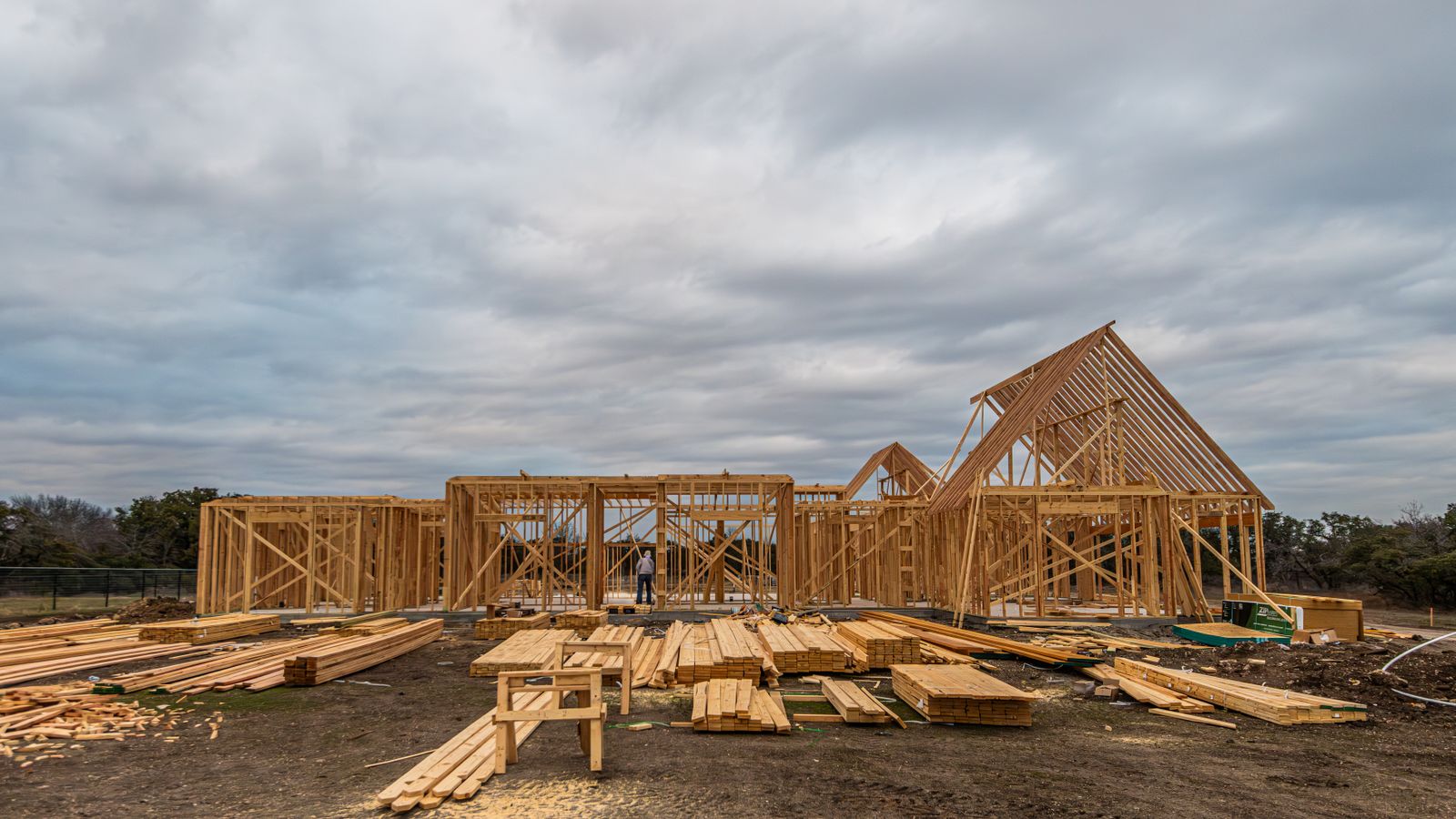 Wood framing of a new house under construction with lumber stacked in the foreground under a cloudy sky