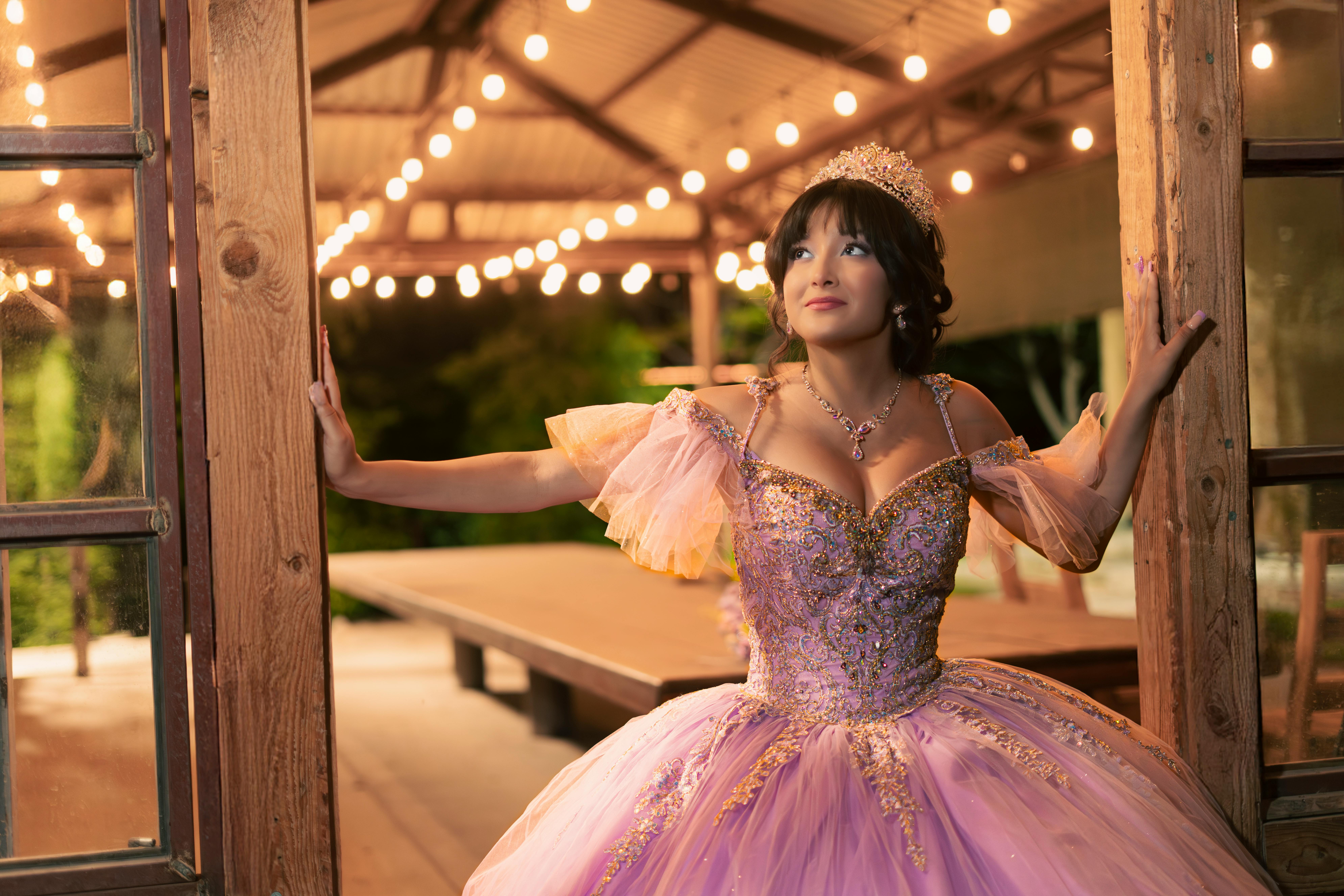 Woman in a sparkling pink ballgown standing under warm fairy lights exuding elegance.