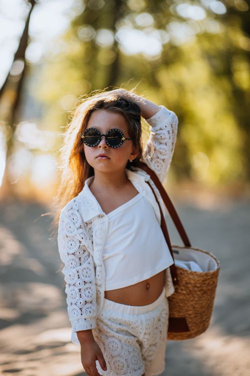 Free Chic young girl with sunglasses and woven basket in sunlit summer park. Stock Photo