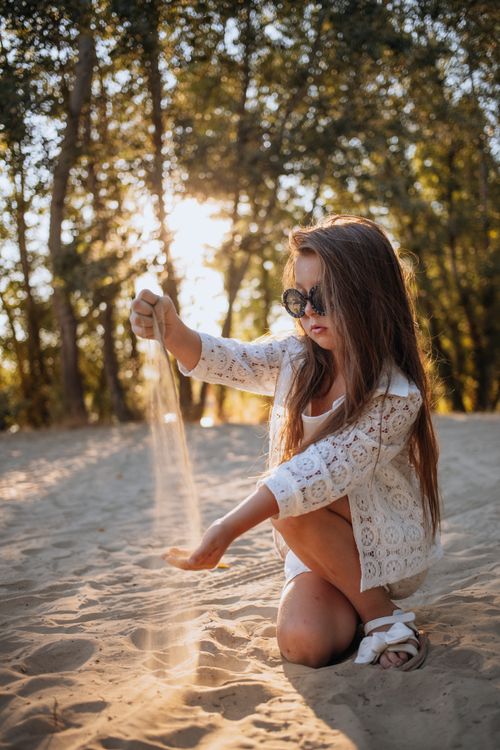 Free A young girl enjoys playing with sand in a sunny forest setting, capturing the essence of summer. Stock Photo