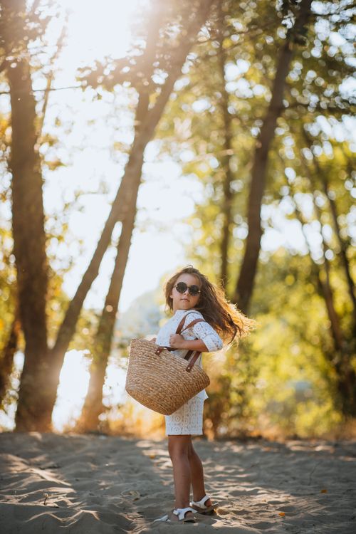 Free A young girl with a woven basket enjoys a sunny day in a forest setting. Stock Photo