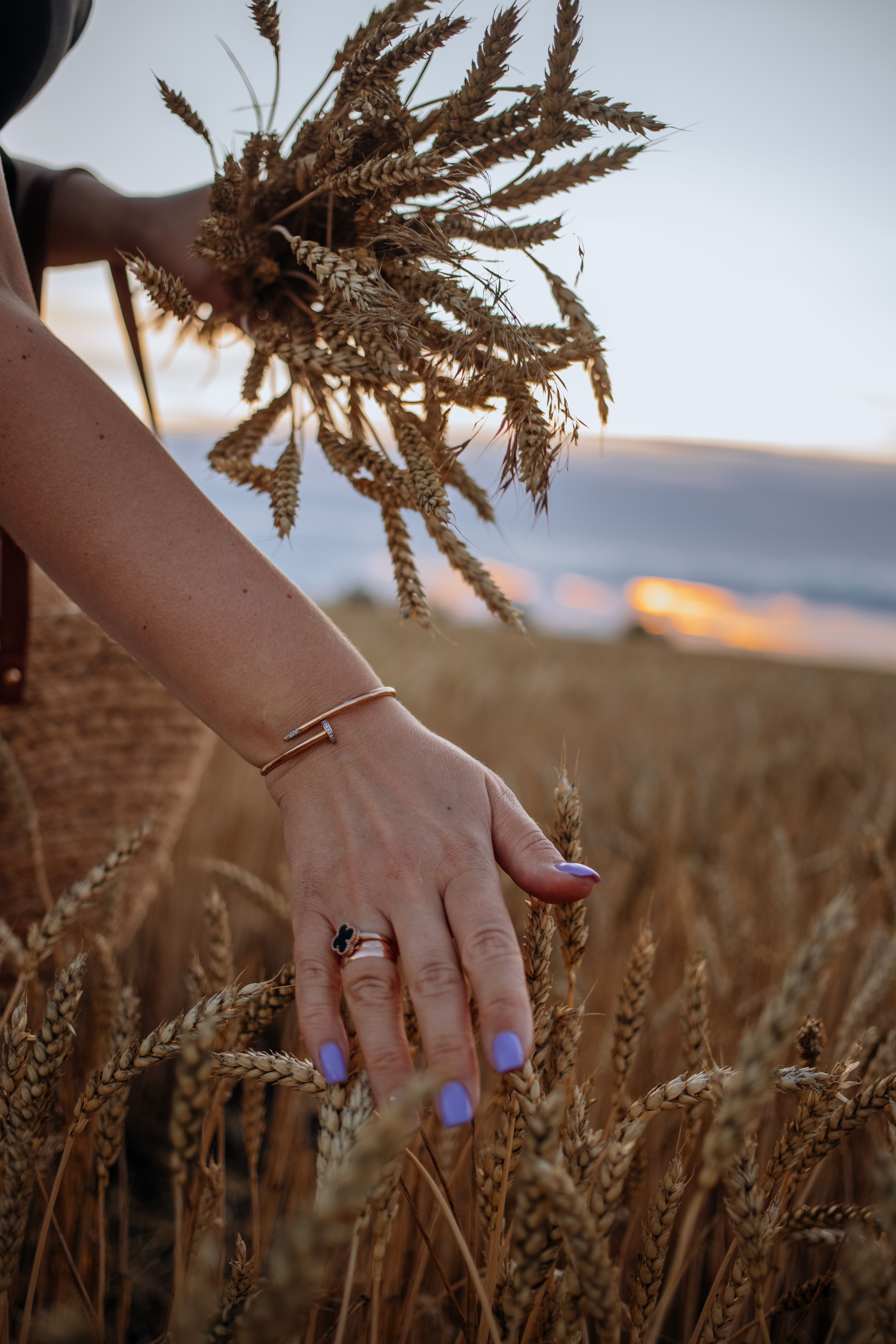 A woman's hand gently touches wheat in a golden field during sunset, capturing summer's serenity.