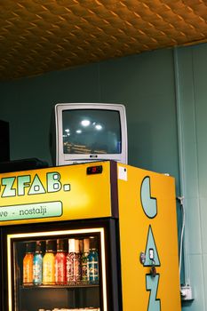 A retro CRT TV placed atop a vibrant yellow beverage cooler with colorful drinks.