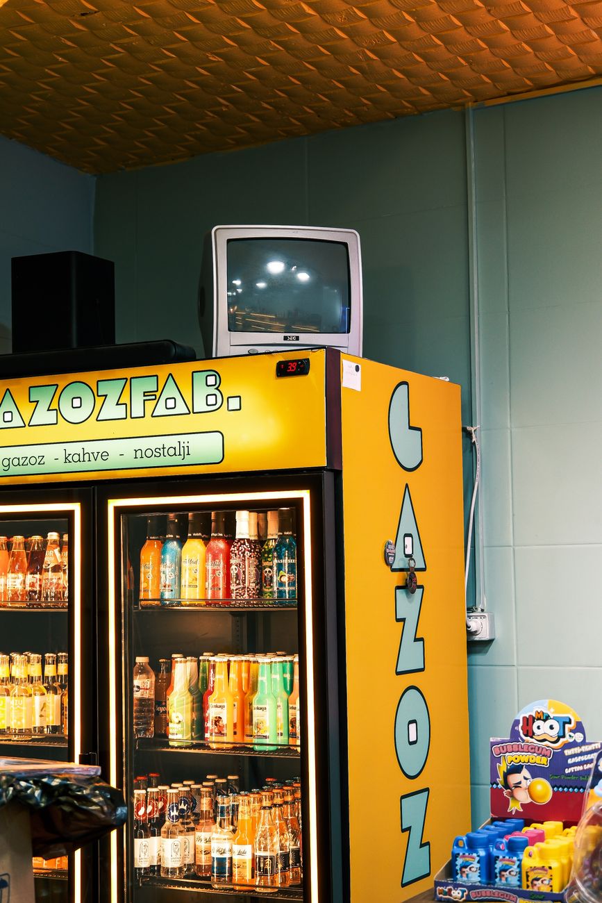 Een nostalgische frisdrankkoelkast met diverse drankjes in een winkel in vintage-stijl, met een retro-tv.