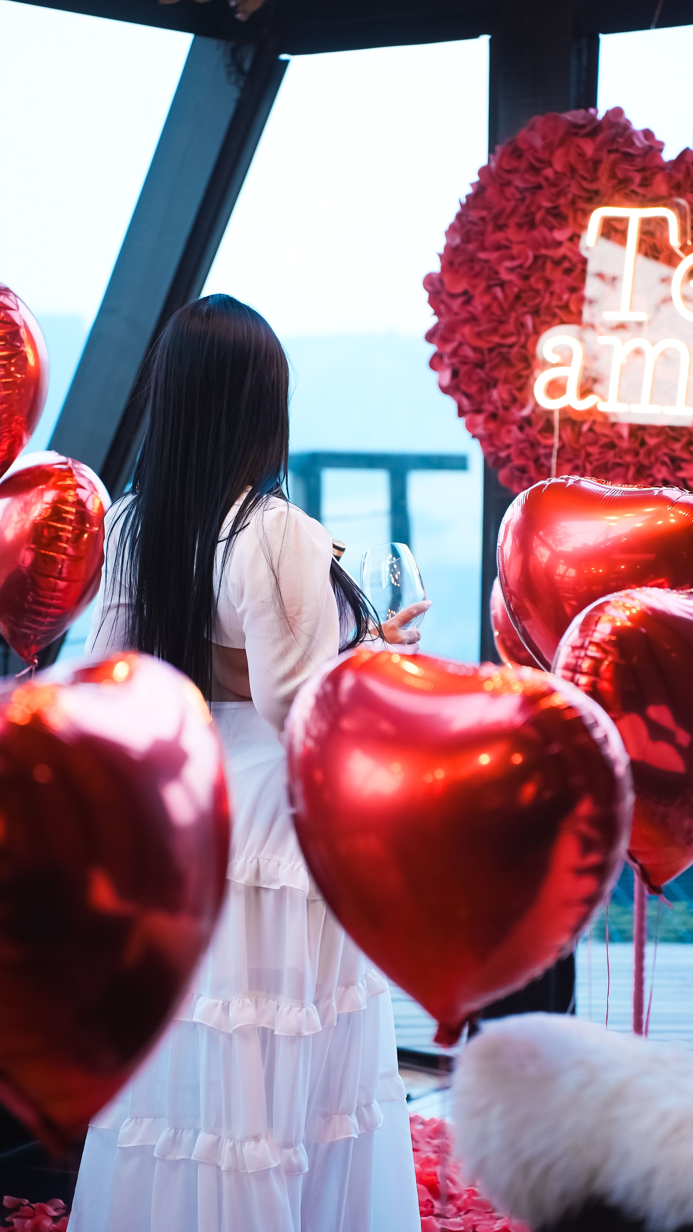 A romantic indoor setup with heart-shaped balloons and a woman in white, creating a loving atmosphere.