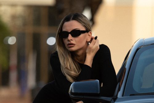 Free Elegant woman in black outfit and sunglasses leaning on a modern car, outdoors. Stock Photo