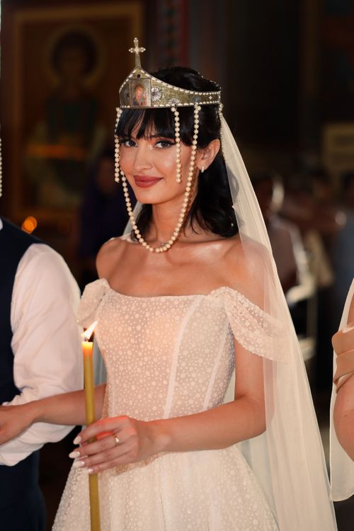 Free A beautiful bride in an Orthodox wedding ceremony holds a candle, adorned in a pearl crown and lace veil. Stock Photo