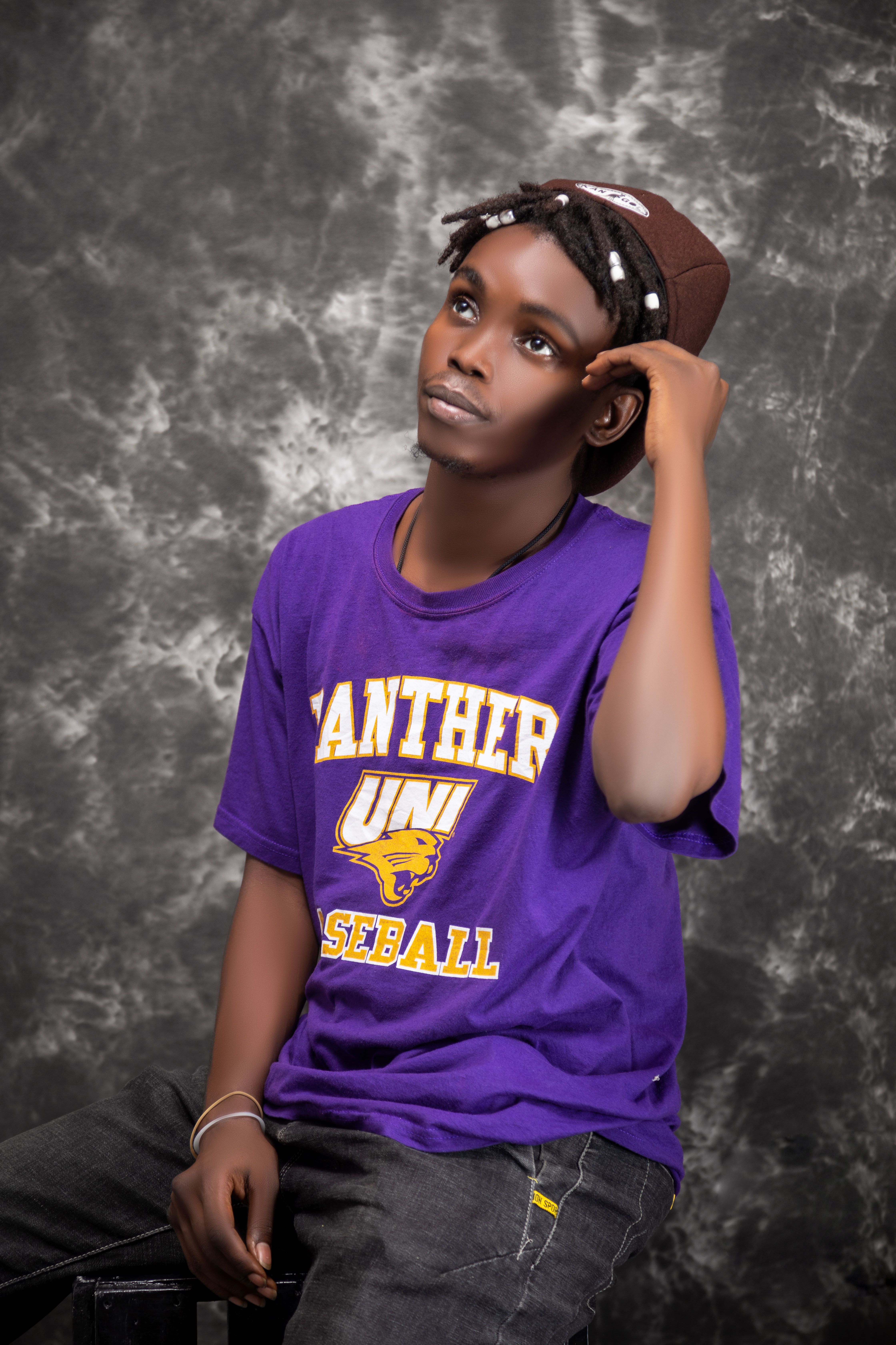 Young adult wearing a purple shirt poses thoughtfully against a marbled backdrop.