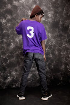 Stylish young man wearing a purple shirt with the number 3, posing creatively indoors.