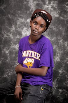 A relaxed studio portrait of a teenager in a purple t-shirt seated in front of a textured backdrop.