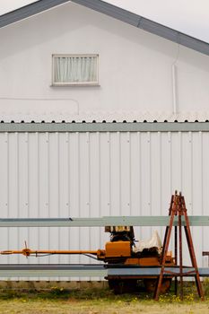 Rusty industrial equipment by a white building exterior, showcasing storage or farm tool setting.