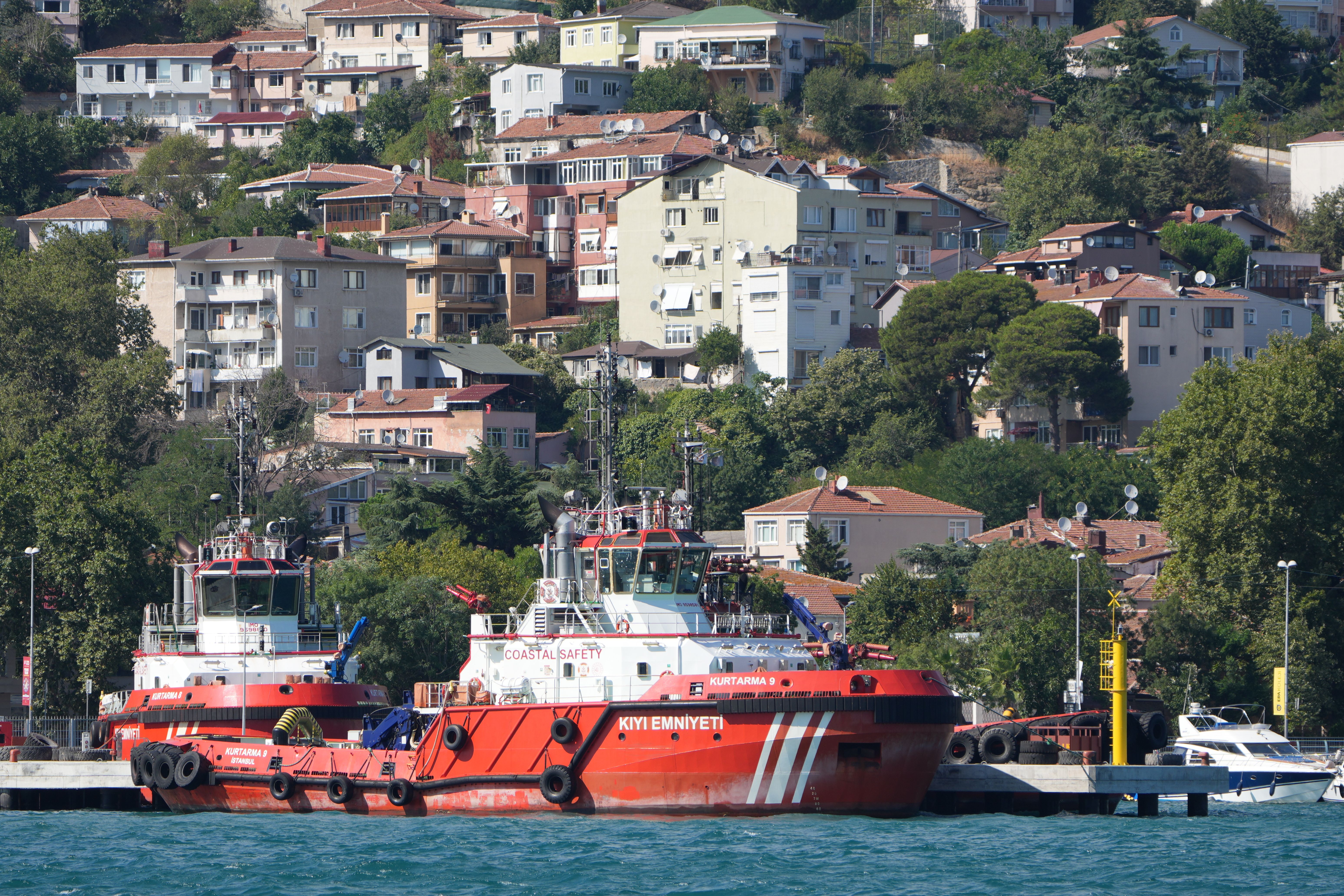 Red coastal safety vessels docked in Istanbul with residential area on the hillside.