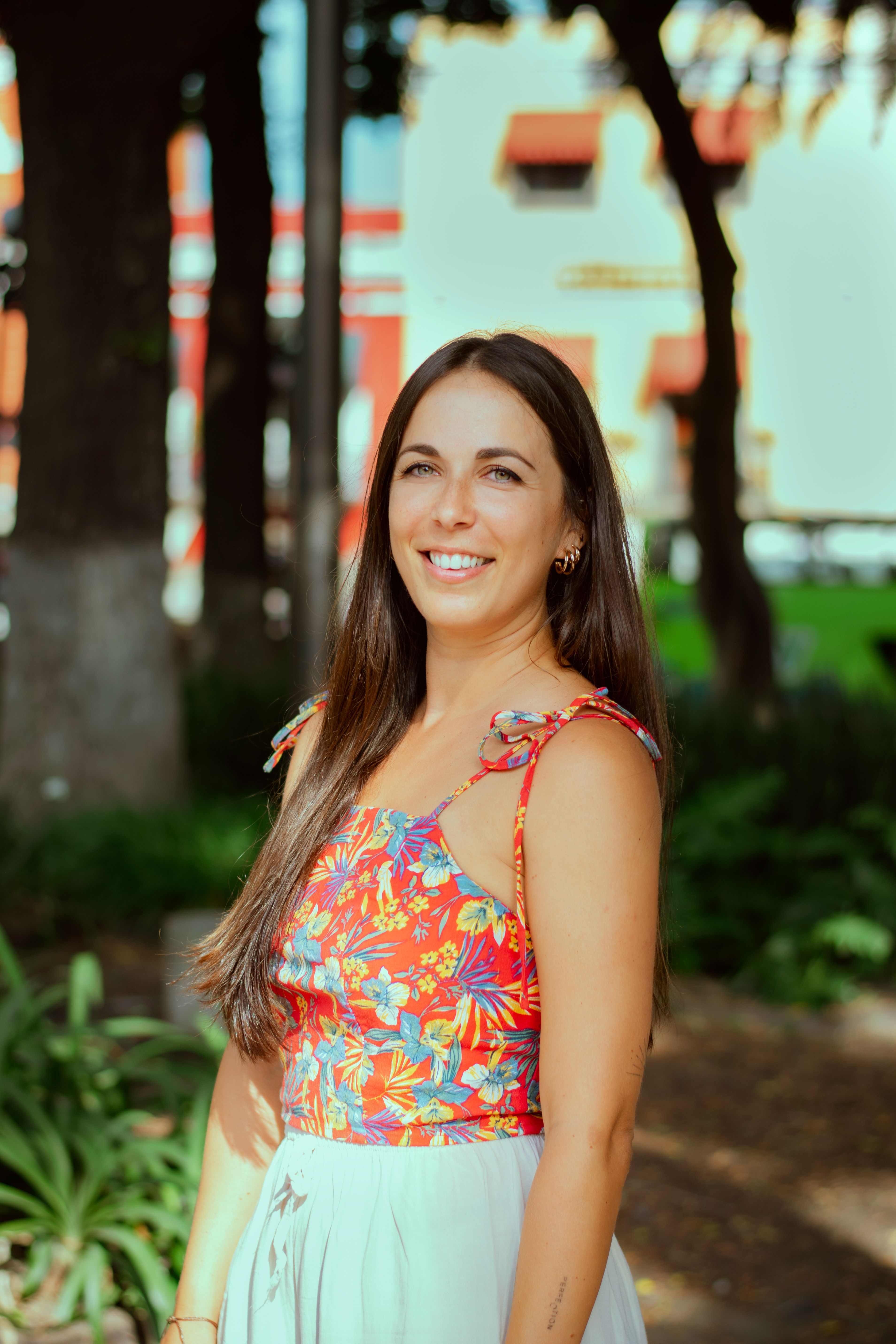 Cheerful woman in a vibrant floral dress enjoying a sunny day outdoors.