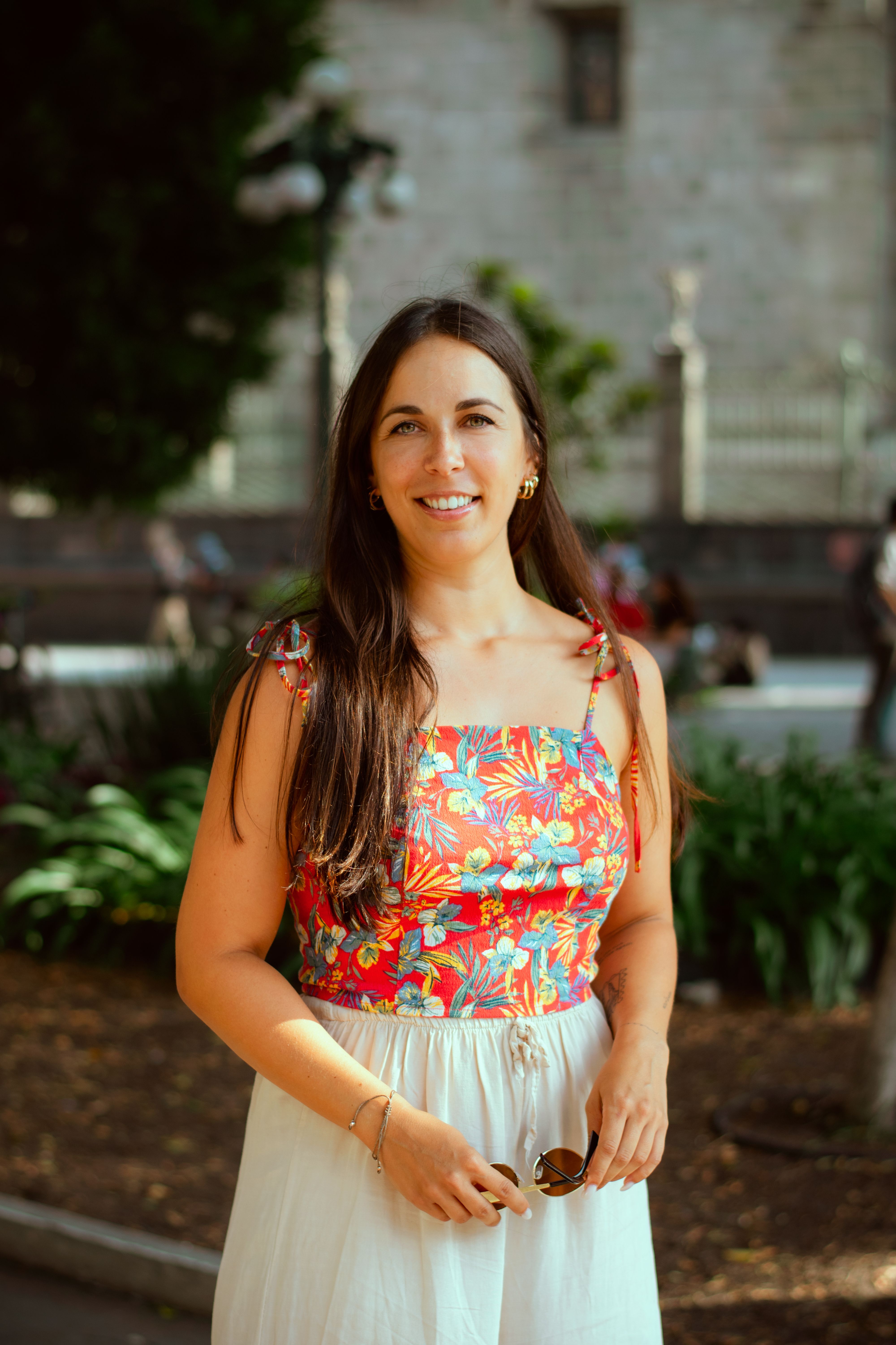Smiling woman in a floral top enjoying a sunny day outdoors, showcasing summer style.
