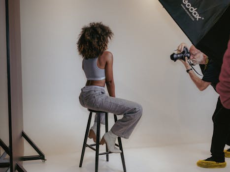 Studio photography session with a model on a stool and photographer in action.