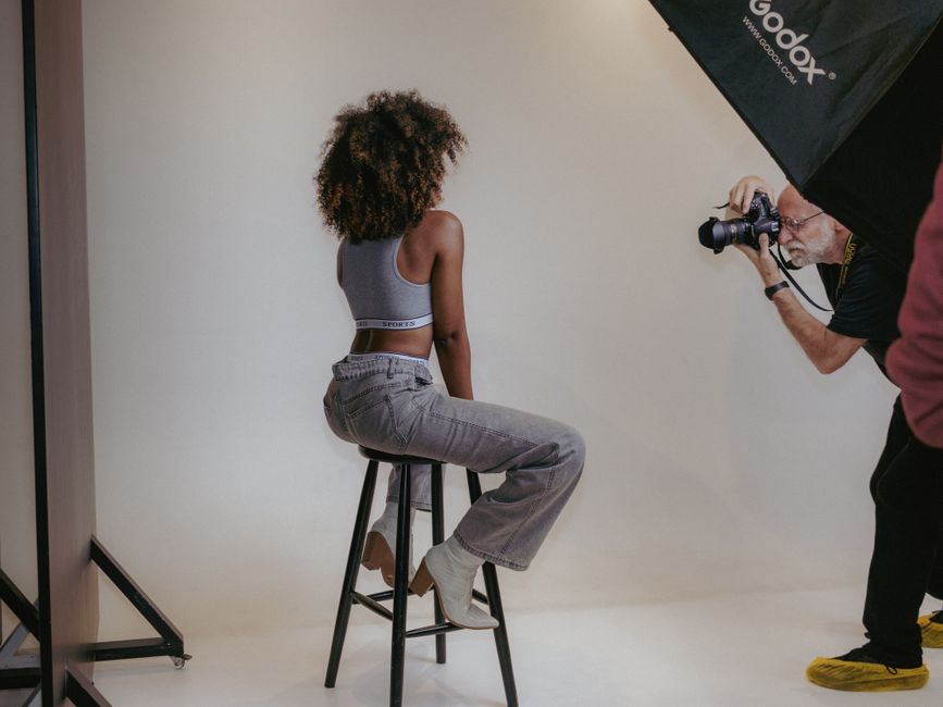 Studio photography session with a model on a stool and photographer in action.